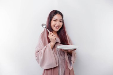 Gülümseyen Asyalı Müslüman bir kadın oruç tutuyor, aç ve bir tabağı işaret ediyor.
