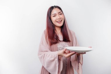 Gülümseyen Asyalı Müslüman bir kadın oruç tutuyor, aç ve bir tabağı işaret ediyor.