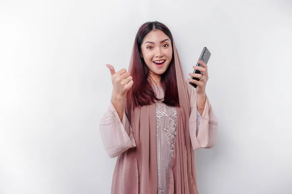 頭皮を身に着けている興奮アジアのイスラム教徒の女性は スマートフォンを保持しながら 承認の親指アップジェスチャーを与えます — ストック写真