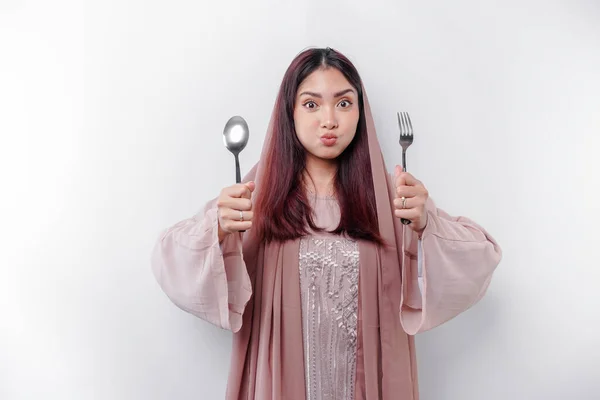 stock image An Asian Muslim woman is fasting and hungry and holding cutlery while looking aside thinking about what to eat