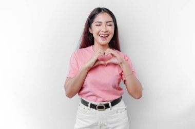 Pembe tişört giyen mutlu bir Asyalı kadın romantik şekiller hisseder. Kalp hareketleri şefkatli duygular ifade eder.