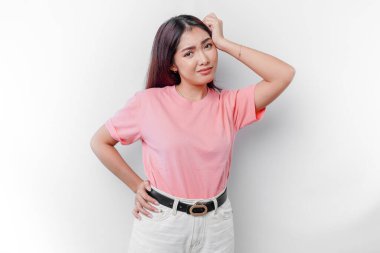 Düşünceli genç bir kadın beyaz arka planla izole edilmiş, kenara bakarken pembe tişört giyiyor.