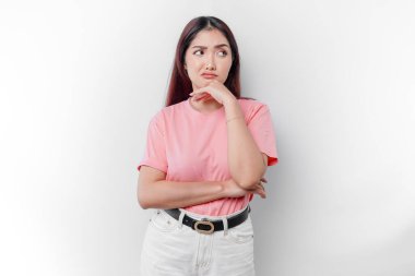 Düşünceli genç bir kadın beyaz arka planla izole edilmiş, kenara bakarken pembe tişört giyiyor.