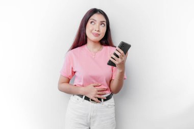 Asyalı bir kadın aç ya da regl ya da mide ağrısı çekiyor. Karnına ve telefonuna dokunuyor.