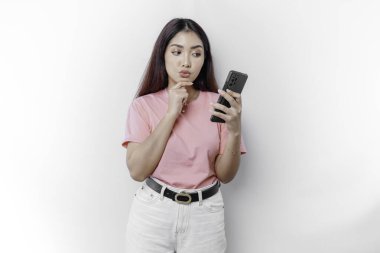 Pembe tişört giyen, çenesini ve telefonunu beyaz arka planda tutan düşünceli genç bir kadın.