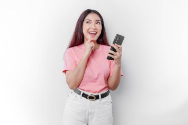 Pembe tişört giyen, çenesini ve telefonunu beyaz arka planda tutan düşünceli genç bir kadın.