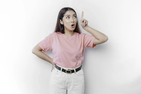 stock image Shocked Asian woman is wearing pink t-shirt, pointing at the copy space on top of her, isolated by white background