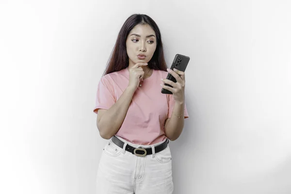 stock image A thoughtful young woman wearing pink t-shirt, holding her chin and her phone isolated by white background