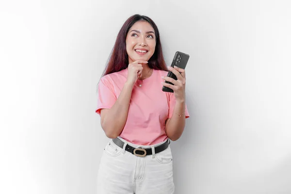 stock image A thoughtful young woman wearing pink t-shirt, holding her chin and her phone isolated by white background