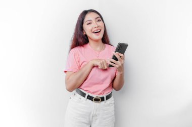 Mutlu bir Asyalı kadının portresi pembe tişört giyiyor ve beyaz arka planla izole edilmiş telefonunu tutuyor.