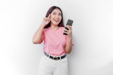Pembe tişört giyen, çenesini ve telefonunu beyaz arka planda tutan düşünceli genç bir kadın.