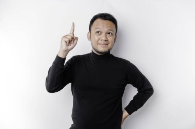 Excited Asian man wearing black shirt pointing at the copy space on top of him, isolated by white background