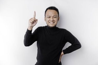 Excited Asian man wearing black shirt pointing at the copy space on top of him, isolated by white background