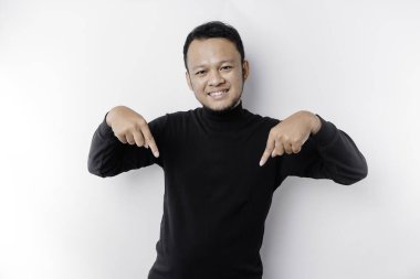 Excited Asian man wearing black shirt pointing at the copy space below him, isolated by white background