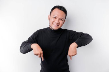 Excited Asian man wearing black shirt pointing at the copy space below him, isolated by white background