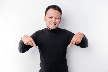 Excited Asian man wearing black shirt pointing at the copy space below him, isolated by white background