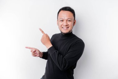 Excited Asian man wearing black shirt pointing at the copy space beside him, isolated by white background