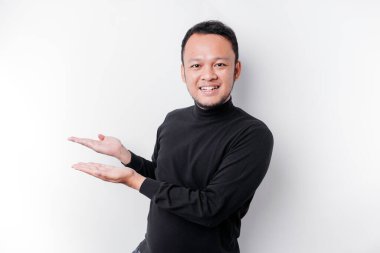 Excited Asian man wearing black shirt pointing at the copy space beside him, isolated by white background