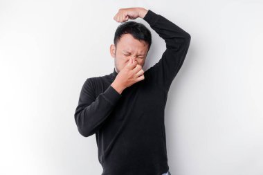 Siyah tişörtlü genç Asyalı adam izole edilmiş beyaz arka plan üzerinde duruyor vücut kokusu, kokuşmuş ve iğrenç, dayanılmaz bir koku. Kötü koku konsepti.