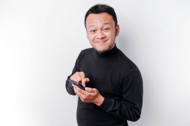 Excited Asian man wearing black shirt smiling while holding his phone, isolated by white background