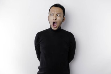 Şok olmuş Asyalı bir adam, ağzı açık, siyah gömlekli, beyaz bir arka planla izole edilmiş.
