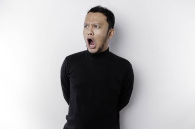 Şok olmuş Asyalı bir adam, ağzı açık, siyah gömlekli, beyaz bir arka planla izole edilmiş.