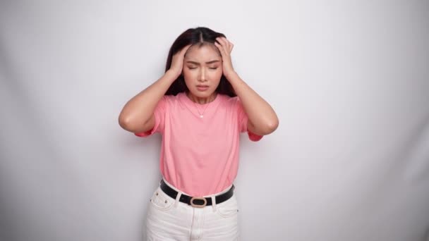 一位心事重重的年轻亚洲女人穿着粉色衬衫 在有着白色背景的工作室里显得很困惑或焦虑 — 图库视频影像