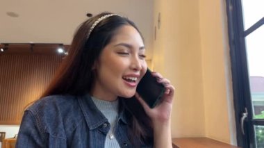 Güzel bir Asyalı kadın bir kafede telefonla konuşuyor.