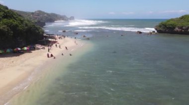 İnsanlar Gunung Kidul, Endonezya 'daki güzel plajlarda gün ışığında mercan kayaları, yeşil deniz yosunları ve ön planda alçak gelgitlerle oynuyorlar.