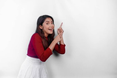 Kırmızı tişört giyen heyecanlı Asyalı kadın, üstündeki fotokopi alanını gösteriyor, beyaz arka planla izole edilmiş.