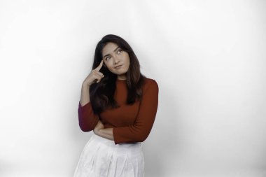 Kırmızı tişört giyen düşünceli genç bir kadın beyaz arka planla izole edilmiş bir şekilde yan tarafa bakıyor.