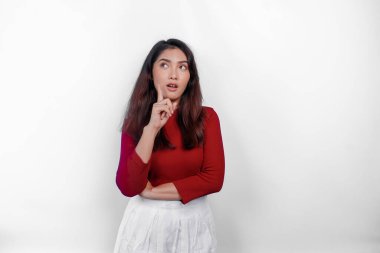 Kırmızı tişört giyen düşünceli genç bir kadın beyaz arka planla izole edilmiş bir şekilde yan tarafa bakıyor.