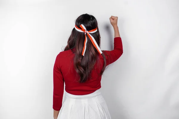 stock image Back view of a young Asian woman with a happy successful gesture wearing red top and flag headband isolated by white background. Indonesia's independence day concept.