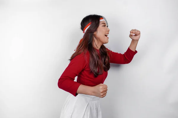 stock image A young Asian woman with a happy successful expression wearing red top and flag headband isolated by white background. Indonesia's independence day concept.