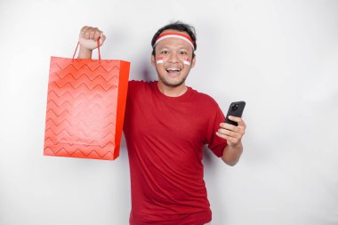 Çekici bir Asyalı elinde online alışveriş çantası ve beyaz arka planda izole edilmiş akıllı telefonu ile heyecanla bekliyor. Endonezya 'nın Bağımsızlık Günü konsepti