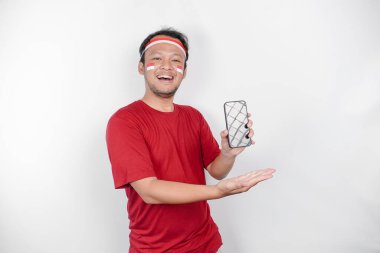 Saçbandı takan ve telefonunu gösteren gülümseyen Asyalı bir adamın portresi, beyaz arka planla izole edilmiş. Endonezya 'nın bağımsızlık günü konsepti