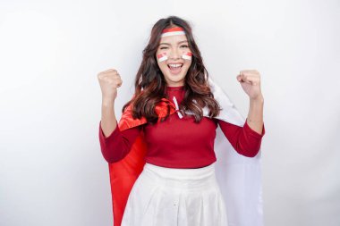 A young Asian woman with a happy successful expression wearing red top and headband while holding Indonesia's flag, isolated by white background. Indonesia's independence day concept.