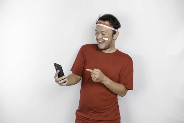 stock image A portrait of a smiling Asian man wearing headband and holding his phone, isolated by white background. Indonesia's independence day concept