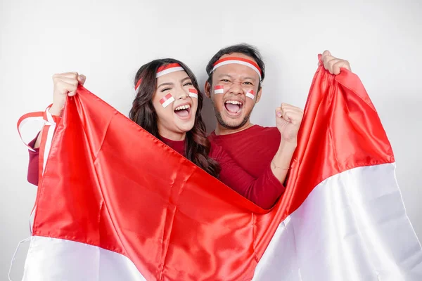 白い背景で孤立したインドネシアの旗を保持しながら 赤いトップとヘッドバンドを身に着けた幸せな表情を持つ若いアジアのカップル インドネシア独立記念日 — ストック写真