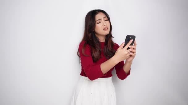 아시아의 여자는 빨간색 티셔츠를 그녀의 전화를 배경에 스러워 보인다 — 비디오