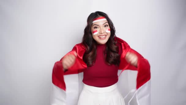 A young Asian woman with a happy successful expression wearing red top and headband while holding Indonesia's flag, isolated by white background. Indonesia's independence day concept.