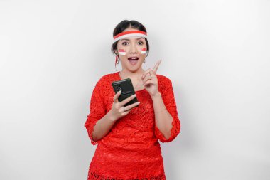 Kırmızı kebaya ve saç bandı takan mutlu bir Asyalı kadın. Telefonunu tutuyor ve beyaz arka planla izole edilmiş fotokopi cihazını üzerine doğrultuyor. Endonezya 'nın bağımsızlık günü