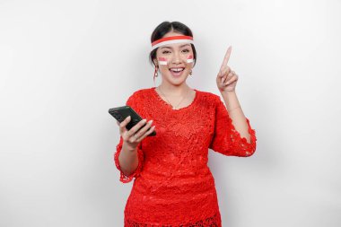 Kırmızı kebaya ve saç bandı takan mutlu bir Asyalı kadın. Telefonunu tutuyor ve beyaz arka planla izole edilmiş fotokopi cihazını üzerine doğrultuyor. Endonezya 'nın bağımsızlık günü