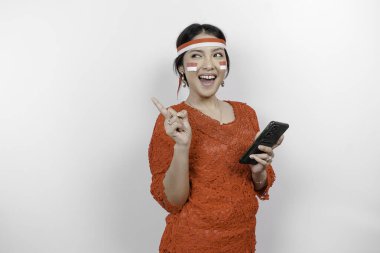 Kırmızı kebaya ve saç bandı takan mutlu bir Asyalı kadın. Telefonunu tutuyor ve beyaz arka planla izole edilmiş fotokopi cihazını üzerine doğrultuyor. Endonezya 'nın bağımsızlık günü