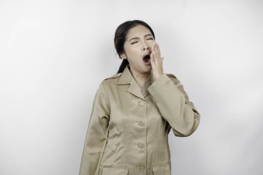 Kahverengi üniforma giyen ve esnerken ağzını eliyle kapatan uykulu Asyalı kadın portresi. Beyaz arkaplanda izole edilmiş resim