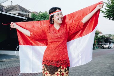 Endonezya Bağımsızlık Günü 'nü kutlamak için elinde Endonezya bayrağı tutan kırmızı kebaya giymiş mutlu Endonezyalı kadın. Açık hava fotoşopu kavramı
