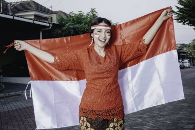Endonezya Bağımsızlık Günü 'nü kutlamak için elinde Endonezya bayrağı tutan kırmızı kebaya giymiş mutlu Endonezyalı kadın. Açık hava fotoşopu kavramı