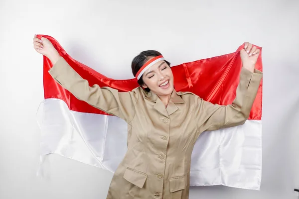 Smiling government worker woman holding Indonesia\'s flag isolated by white background. PNS wearing khaki uniform. Indonesia\'s independence day concept.