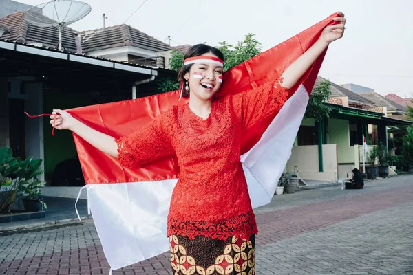 インドネシア独立記念日にインドネシアの旗を掲げた赤いケバヤを着たインドネシア人女性の笑顔 アウトドア写真撮影コンセプト — ストック写真