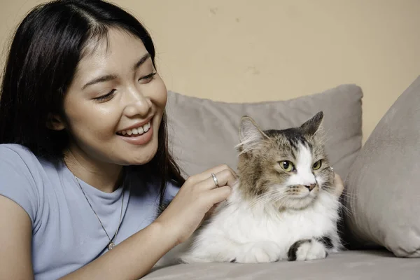 Pretty Asian woman hug a cat and sit on couch with happy emotion. Adorable domestic pet concept.